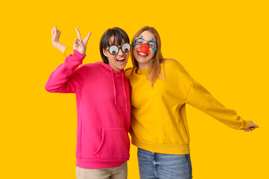Beautiful young happy women in funny disguise on yellow background. April Fools Day celebration