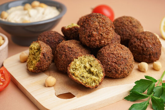 Wooden board with delicious falafel balls and parsley on beige background, closeup