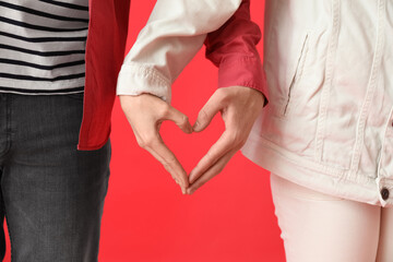 Young couple making heart with their hands on red background, closeup