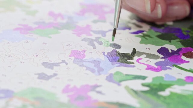 Close up of a beginner practicing painting techniques on a numbered canvas. Developing fine motor skills and artistic ability through guided paint-by-numbers system.