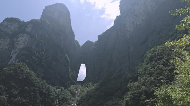 Natural rock arch framed by towering cliffs at Tianmen Mountain Zhangjiajie China, upward angled background