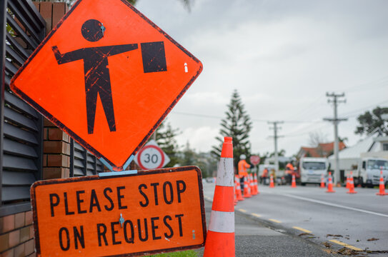 Please Stop on Request road sign by the road. Unrecognizable workers holding STOP sign. Auckland.