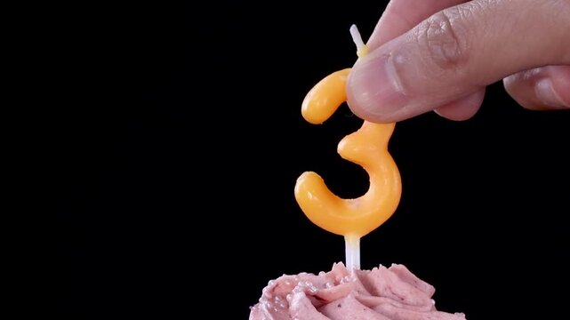 Hand Placing Yellow Number Three Candle into Pink Frosted Cupcake
