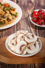 Fototapeta premium Fresh Sliced White Mushrooms on Plate with Tomatoes and Cooked Dish on Rustic Wooden Table