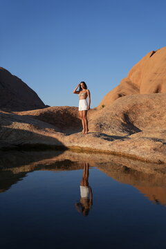 Woman in white shorts standing beside a rock pool and reflecting