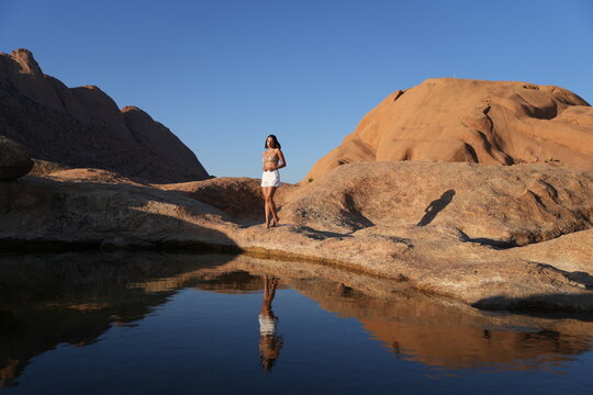 Woman in white shorts standing beside a rock pool and reflecting