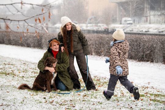 mother and daughters of different ages play with dog in snowy park