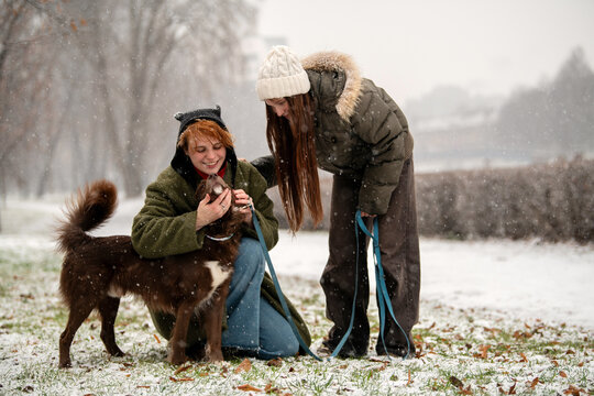 mother and teenage daughter play with their dog in a snowy park.