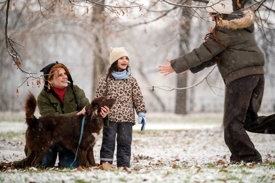 mother and daughters of different ages play with dog in snowy park