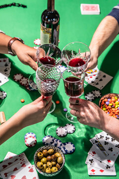 Friends toasting wine while playing poker on green table