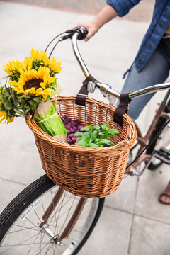 Person cycling bicycle with front basket of sunflowers and produce