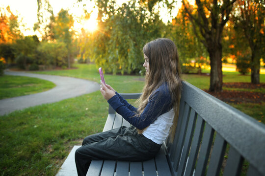 Side view teen girl looking at cellular phone sitting on bench s