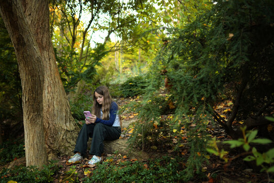 Young teen girl sitting outdoors looking at pink cell phone