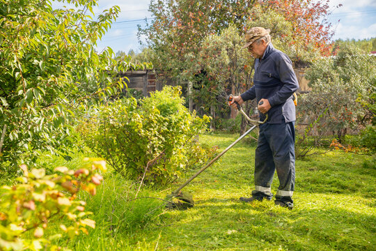 Senior man uses grass trimmer to cut overgrown lawn in his backyard