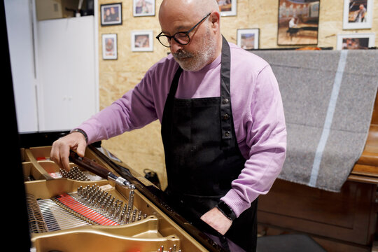 Piano technician tuning grand piano in workshop