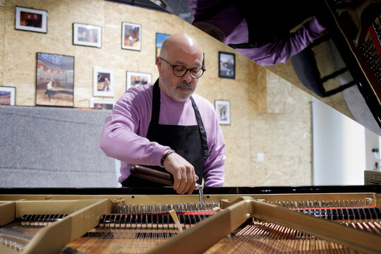 Piano technician tuning grand piano in workshop