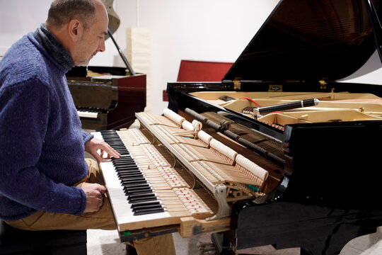 Piano technician testing keys on grand piano
