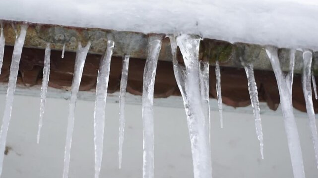 Sharp transparent icicles hanging from snowy house roof edge