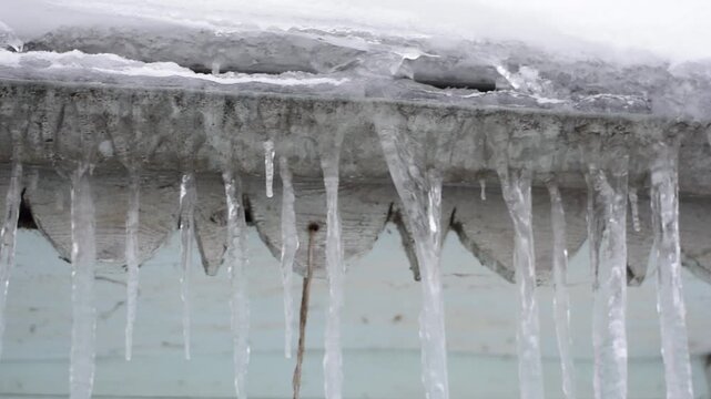 Long transparent icicles hanging from the edge of a snowy roof in winter season