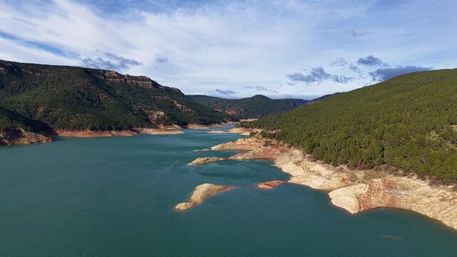 Aerial view of Embalse de Benageber on the Turia River, showing mountain reservoir geometry, exposed shorelines, forested slopes, and managed water storage infrastructure.