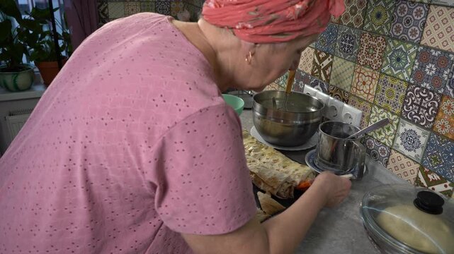 Elderly woman cooking food at home. Brush the top of the pies with eggs