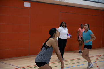 Obraz premium Diverse female teammates practicing volleyball in gym in sportswear with coach holding volleyball