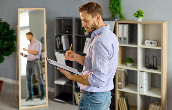 Preparation for job interview, rehearsal of public presentation of man by mirror at home. Male presenter holding clipboard and pencil to write notes and practice confident speech by reflection