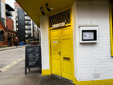 Bright yellow Maricarmen spanish tapas bar door entrance in Manchester cafe with chalkboard menu on cobbled street