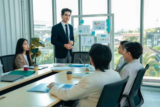 Project director reviews quarterly results with management team in conference setting. Board displays statistics while members analyze opportunities. Performance evaluation, business strategy idea.