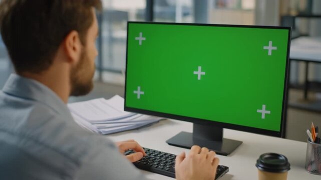 Man working on computer with green screen display in modern office environment from behind viewpoint