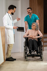 Doctor consulting senior patient in wheelchair with male nurse