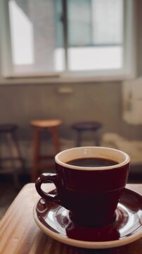 Steaming hot cup of black coffee with rising vapor on a wooden table, morning light
