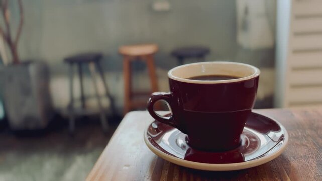 Steaming hot cup of black coffee with rising vapor on a wooden table, morning light