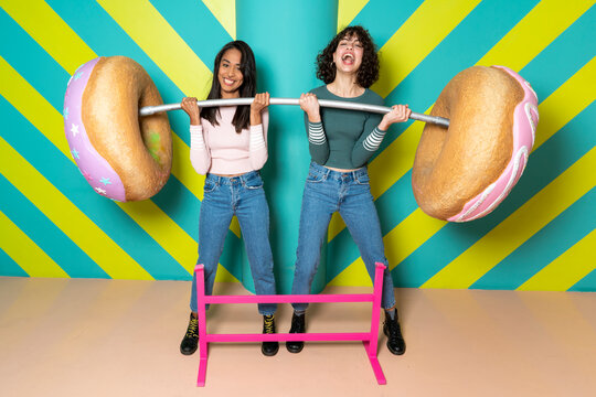 Two happy young women at an indoor theme park having fun with oversized donuts