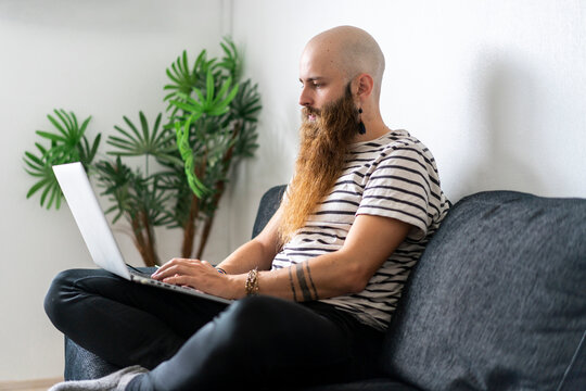 Hipster sitting on couch at home using laptop