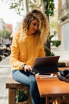 Beautiful blond female student using digital tablet while sitting at sidewalk cafe in city