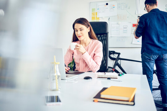 Woman working at desk in office with colleague in background