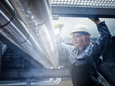 Craftswoman wearing hard hat working at pipe