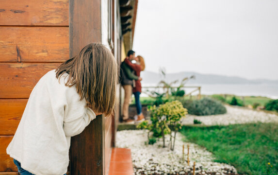 Back view of little girl spying couple in love kissing next to wooden house