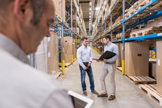 Two men with folder talking in factory warehouse