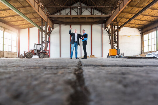 Two businessmen with documents talking in old industrial hall