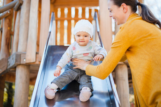 Portrait of baby girl sitting on shute on playground being held by her mother