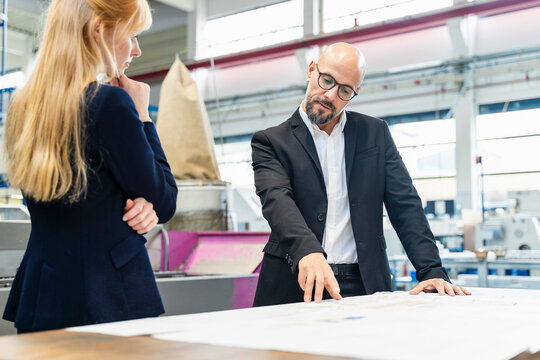 Businessman and businesswoman looking at plan on table in factory