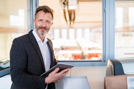 Portrait of businessman using tablet at the window with factory background