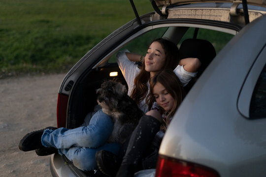 Two sisters in opened boot of parked car watching sunset