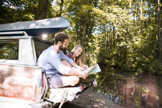 Smiling young couple with map and canoe in car at a brook