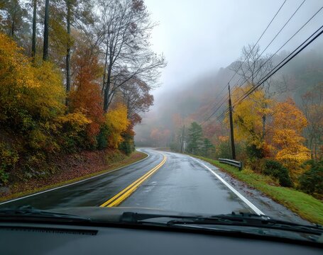 View from a car on a winding road through autumn foliage in dense, foggy mountains