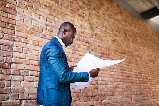 Businessman studying plan at brick wall