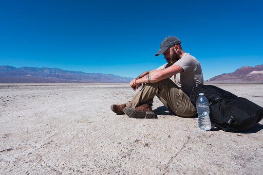 USA, California, Death Valley, man sitting on ground in the desert having a rest