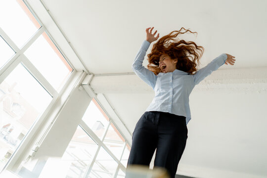 Redheaded woman standing on desk in a loft moving and screaming